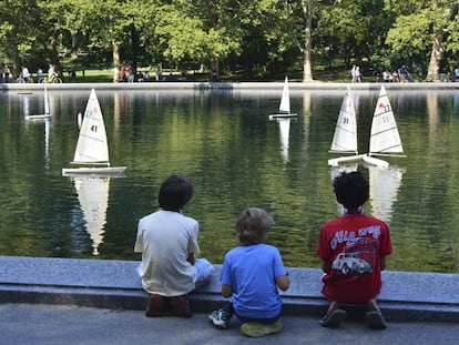 Tres niños miran unos maquetas de barcos navegar en un estanque.